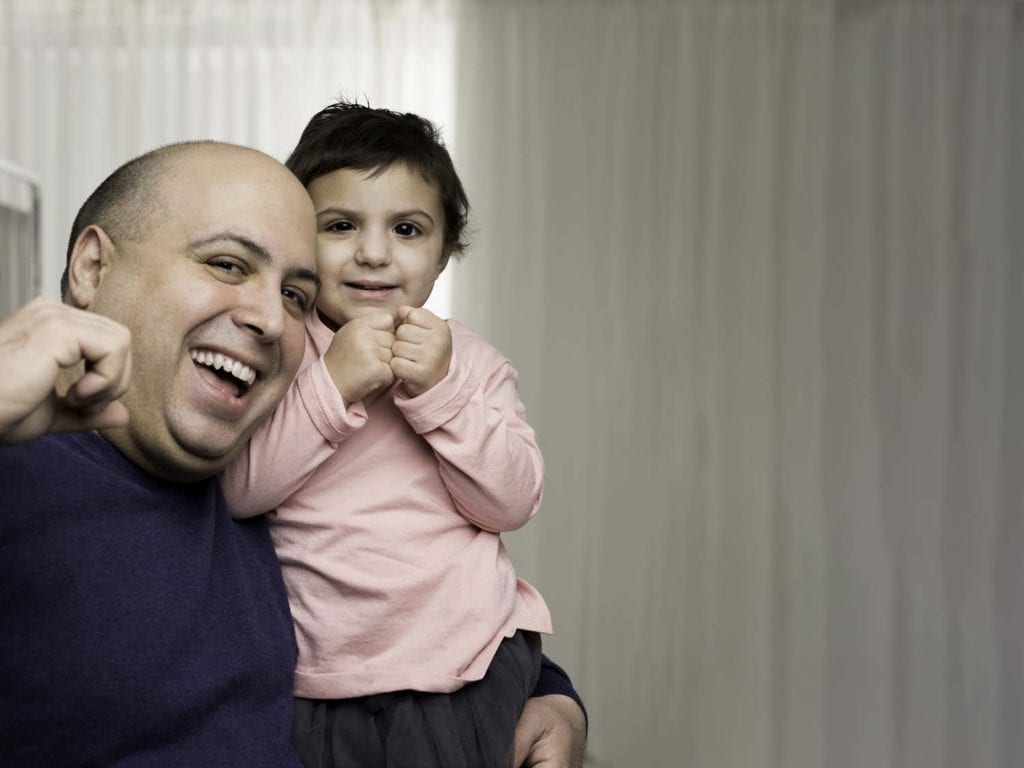 A bald man holding a child with cancer.