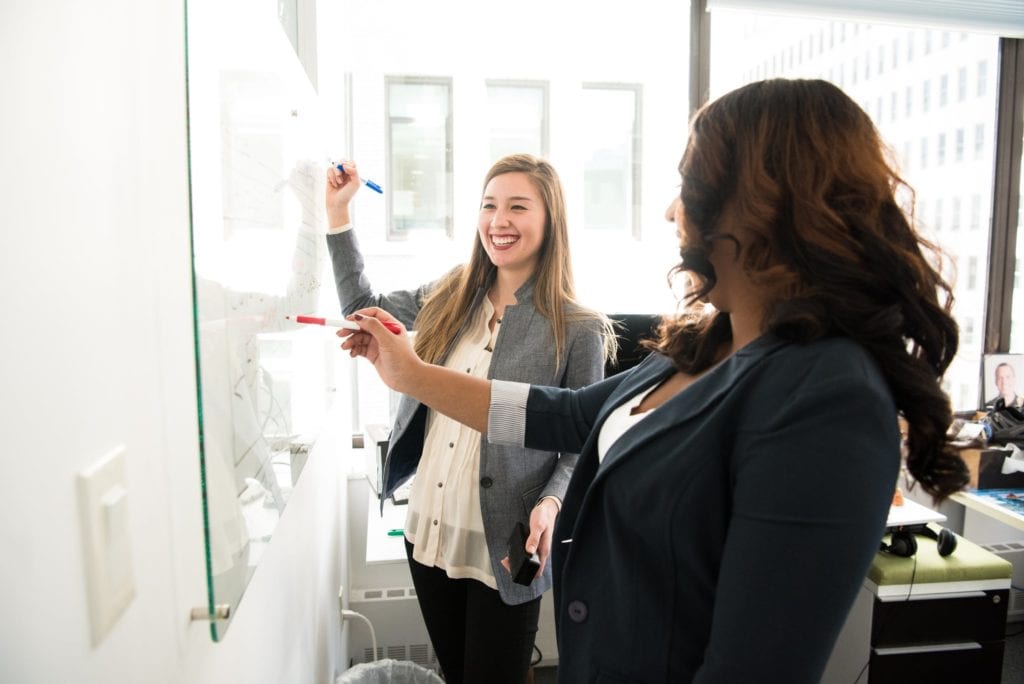Two women at a white board in a business setting