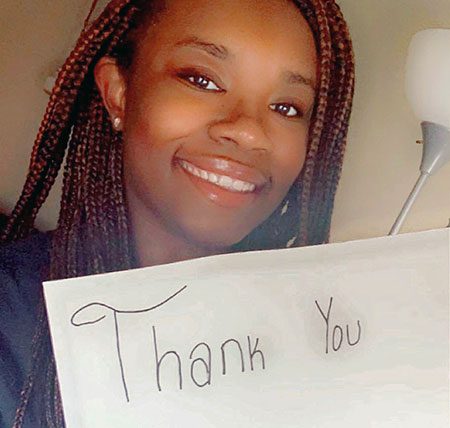 Gabrielle smiles and holds up a thank you sign.