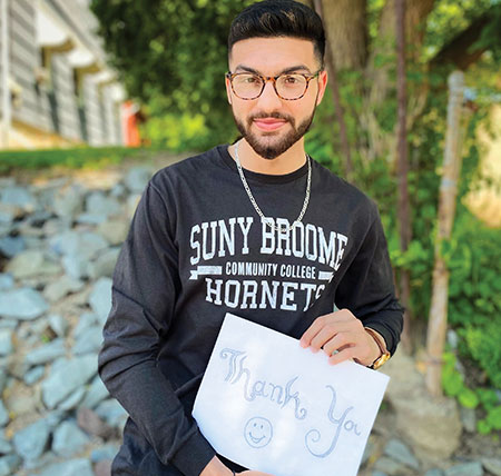 Faisal wears a SUNY Broome Hornet shirt and holds a Thank You sign