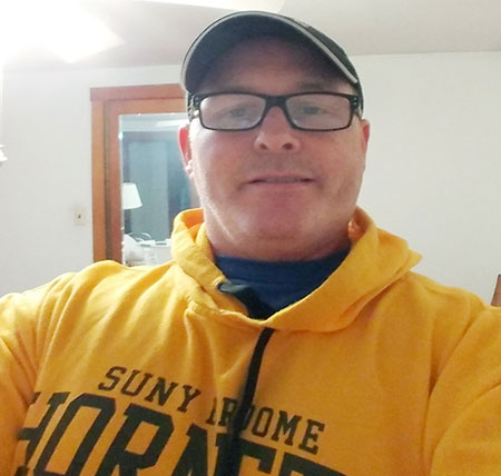 Nathan, wearing a SUNY Broome Hornet sweatshirt, smiles.