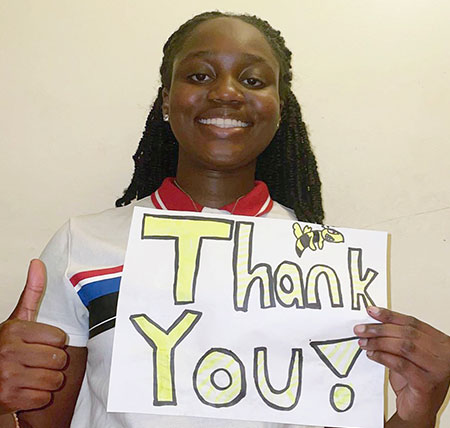 Melina gives a thumbs up as she holds a sign with a hand-drawn Stinger and the words "Thank you".