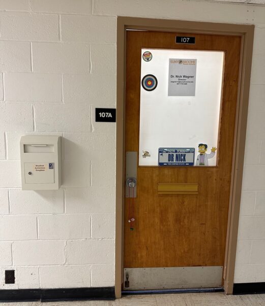 Student Activities office door in Old Science room 107A. Dropbox is on the left side of the door.
