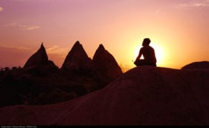 Image of a man meditating on a mountain framed by the sunset