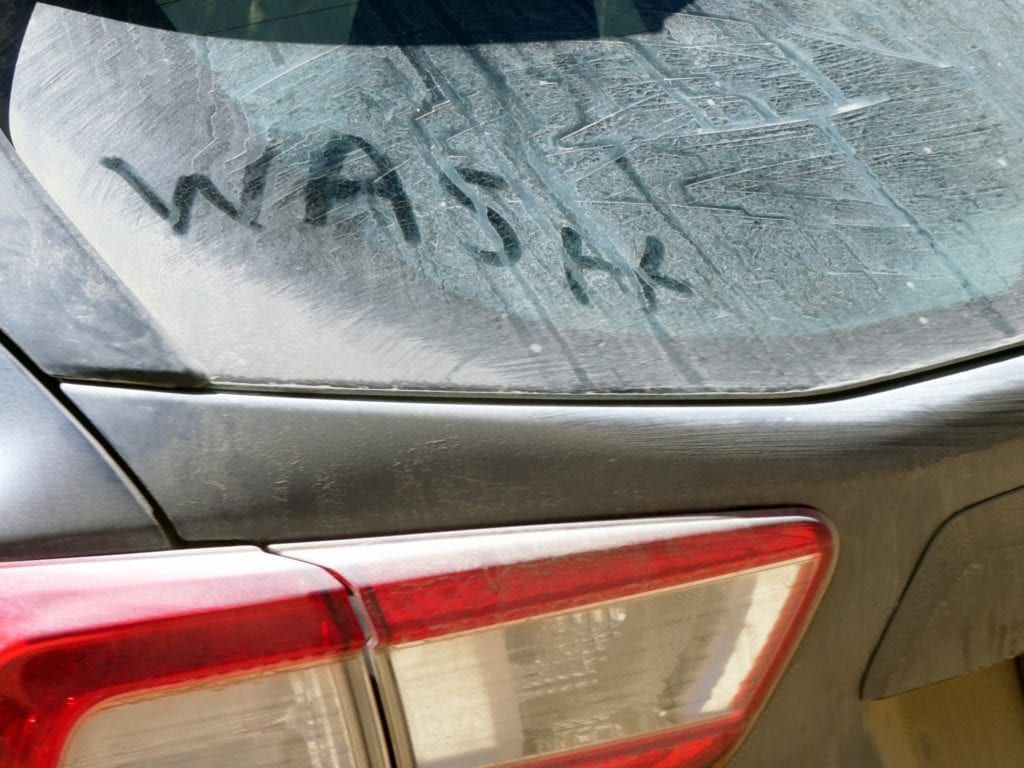 A filthy car with the word "wash" on it