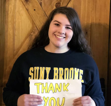Chelsea wears a SUNY Broome T-shirt and a smile as she holds a handwritten "Thank You" sign.