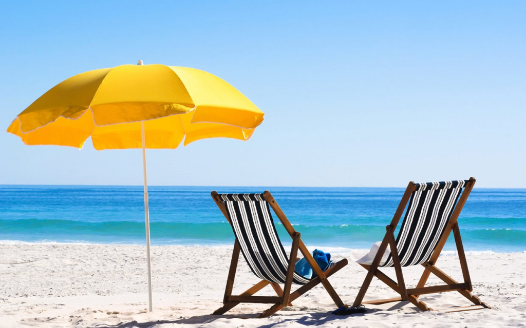Beach scene with ocean, umbrella, and two beach chairs.