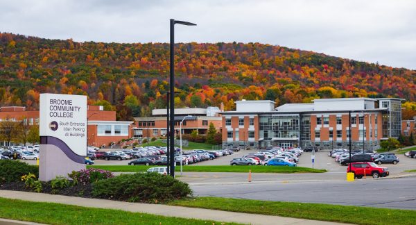 SUNY Broome Campus south entrance sign with fall colored trees on the hill behind campus