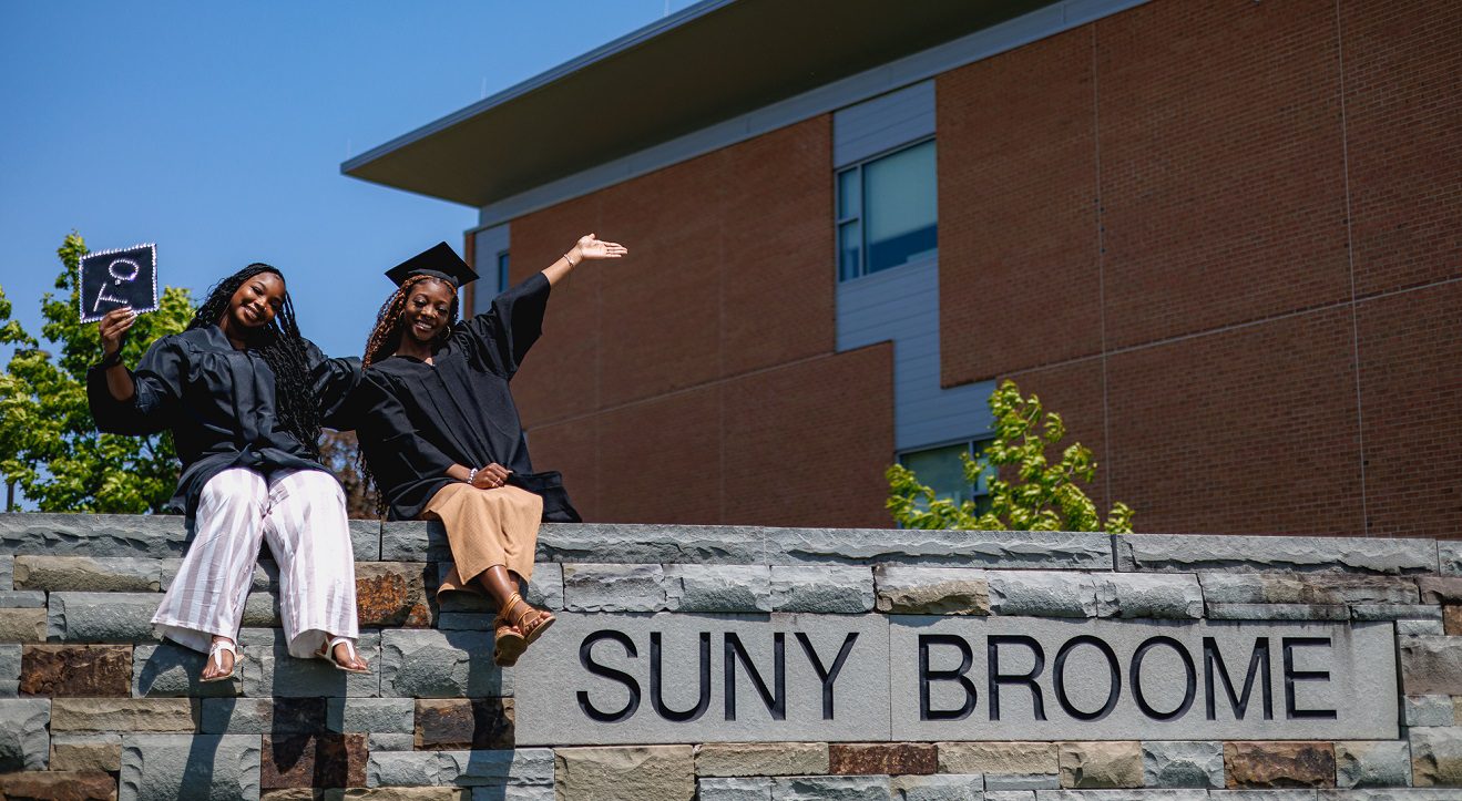 SUNY Broome graduates on the rock wall with SUNY Broome sign.